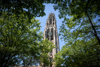 Harkness Tower through green leafy trees against a blue sky