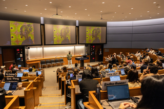 Lecture classroom with students in tiered seating listening to a lecture at the front of the room.