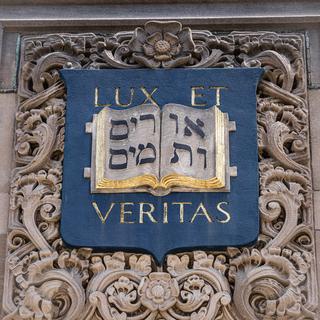 Close up of a stone carving of Yale's coat of arms features an open book and Yale's motto, Lux et Veritas